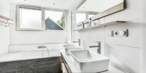Modern white bathroom with double sinks, bathtub, and natural light