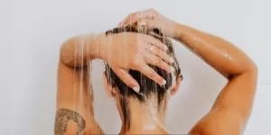 Person washing their hair under a running shower in a modern bathroom